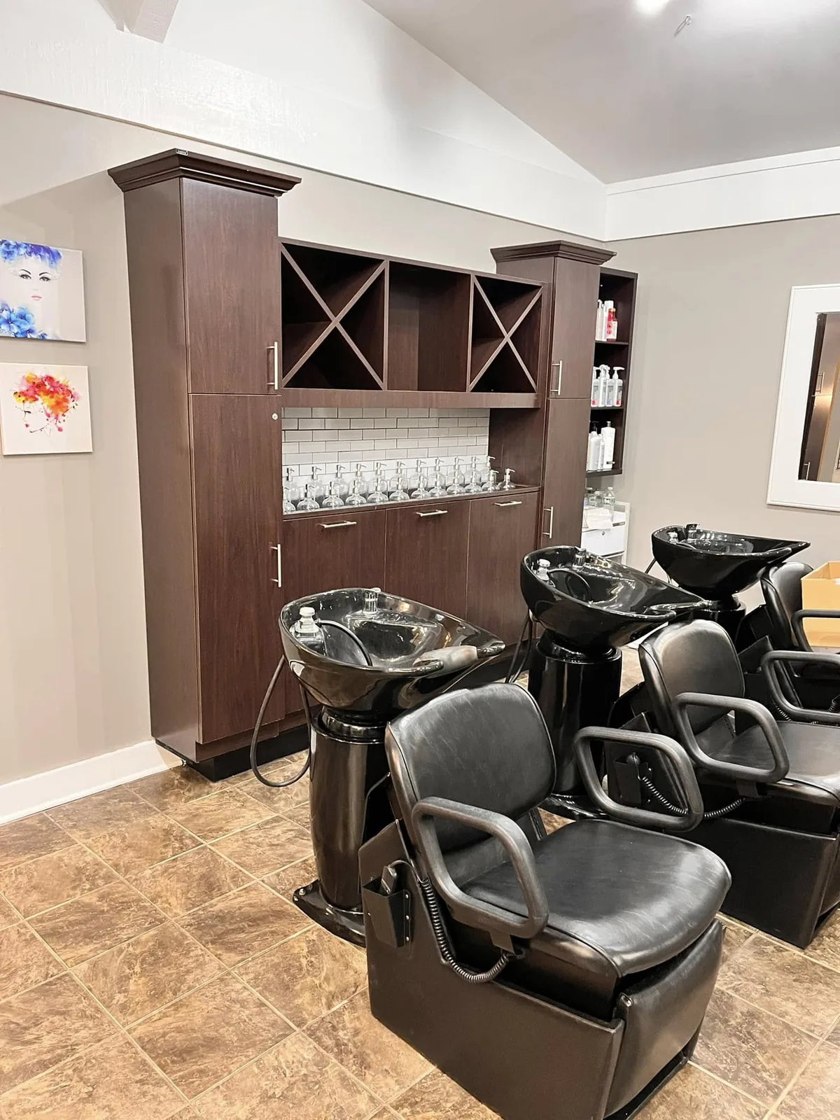 Two shampoo chairs at black sinks beside a dark wood cabinet